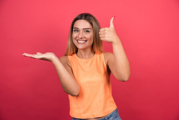 Pretty young woman making thumbs up on red wall. 