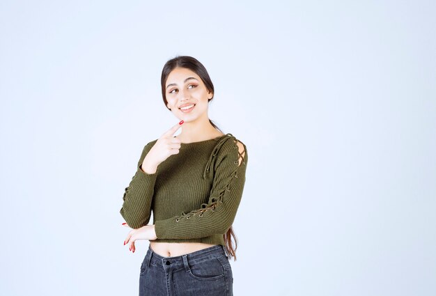 Pretty young woman pointing at her side on white wall