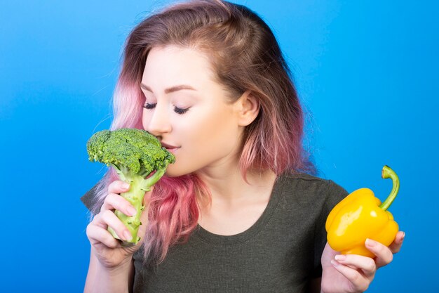 Pretty young woman smelling fresh broccoli in her right hand