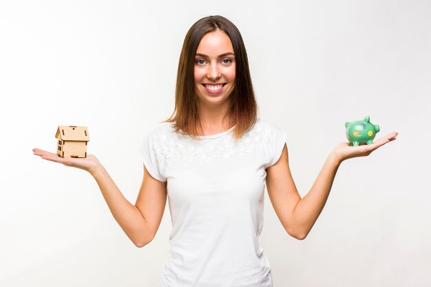 Pretty young woman with a cottage and a piggy bank