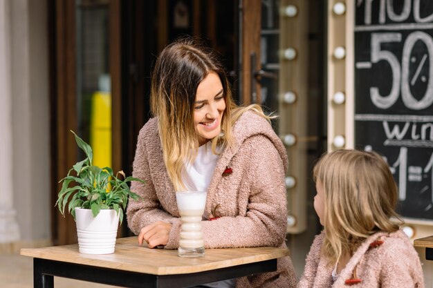 Free photo pretty young woman with little charming daughter dressed in warm sweaters are sitting in cafeteria