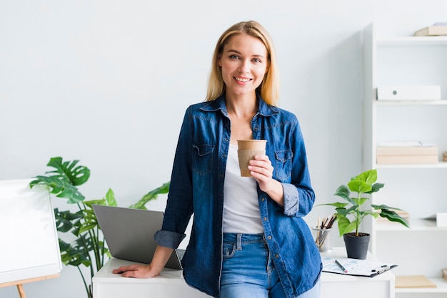 Pretty young woman with paper cup in workplace