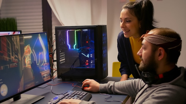 Pro gamer couple playing first person video game on powerful computer wearing professional headphones. Videogamer streaming gameplay cyber game sitting on gaming chair using RGB equipment