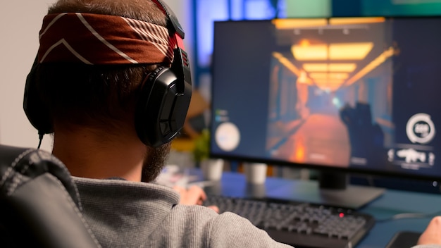 Free photo pro gamer playing on powerful computer first person shooter video game during live championship, wearing headphones. competitive player streaming video game tournament using professional equipment