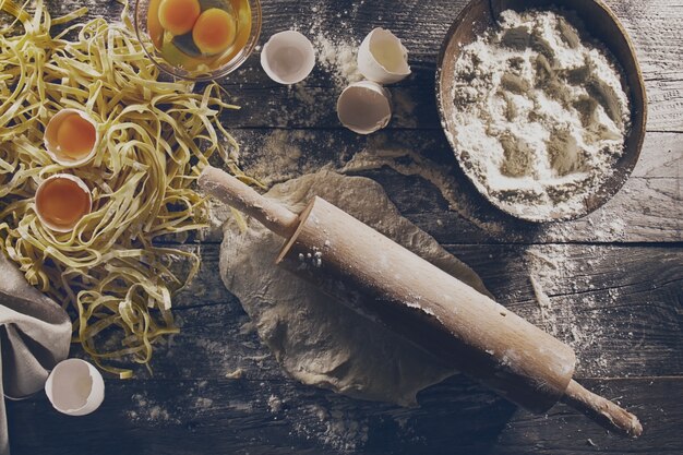 Process of cooking pasta with raw fresh ingredients for classic italian food - raw eggs, flour on wooden table. Top View. Toning.