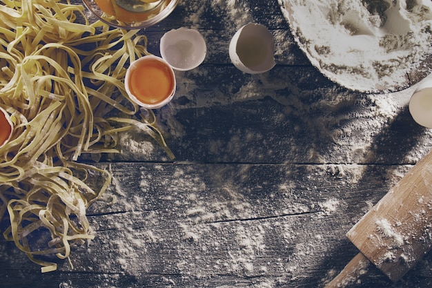 Free Photo process of cooking pasta with raw fresh ingredients for classic italian food - raw eggs, flour on wooden table. top view. toning.