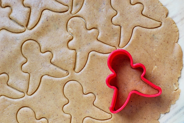 Free photo process of dealing with gingerbread man cookies, use red gingerbread man mold cutting gingerbread dough on baking paper around colorful cookie cutters on white wooden table. top view