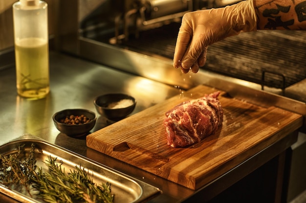 Free photo process of preparing beef steak in professional restaurant kitchen chef in white glove salting meat using such ingredients as seasonings pepper oil and rosemary for spicy taste