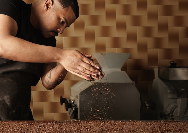 Free photo professional baker pours grained nuts on mold filled with melted chocolate mass. preparation of tasty cake from organic chocolate in artisan confectionery for sale