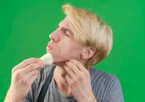 Free photo professional barber man in apron holding shaving brush touching his face with it looking displeased