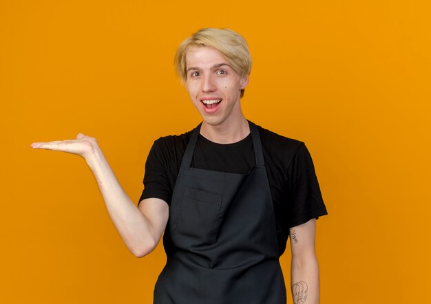 Professional barber man in apron looking smiling presenting copy space with arm of hand standing