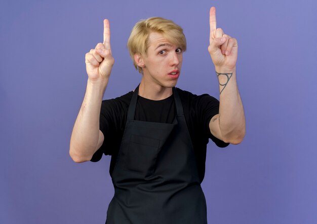 Professional barber man in apron pointing with index fingers up 