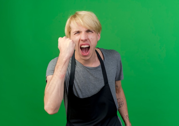 Free Photo professional barber man in apron showing fist to camera with angry face shouting with aggressive expression 