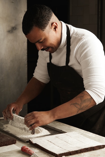 Free Photo professional black conditer puts piece of tasty chocolate cake in sugar powder in his artisan confectionery