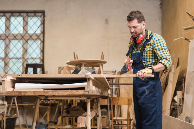 Professional carpenter cutting the wooden plank with handsaw in the workshop