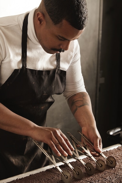 Free photo professional chef black man uses old vintage separator to mark pieces on freshly baked chocolate cake