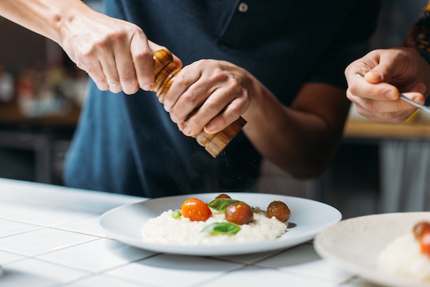 Professional chef prepares amazing tasty steaming dish of italian parmesan risotto at designer hipster kitchen