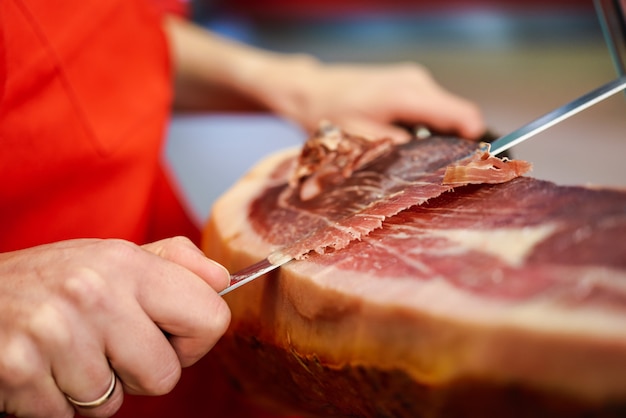 Professional cutter carving slices from a whole bone-in serrano ham