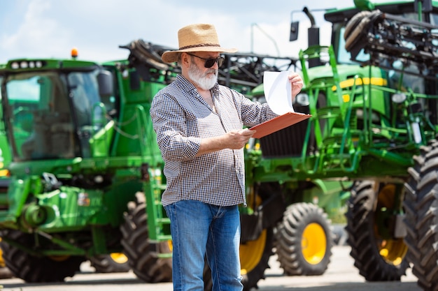 Free photo professional farmer with a modern tractor at work with documents. looks sunshine. agriculture, exhibition, machinery, plant production. senior man near his machine.