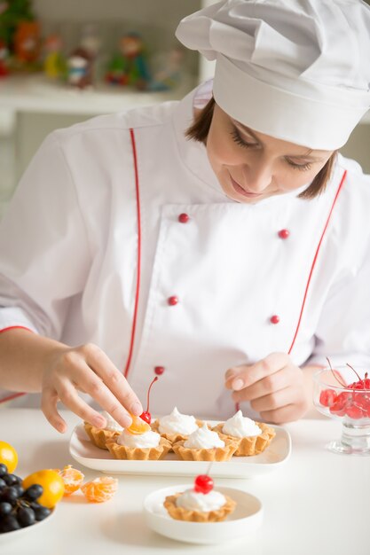 Professional female confectioner decorating mini fruit tarts