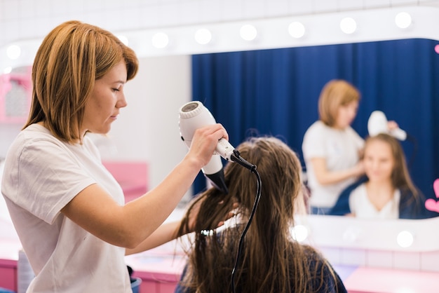 Professional female hairdresser drying woman's hair styling using blow dryer at the hairdressing saloon salon