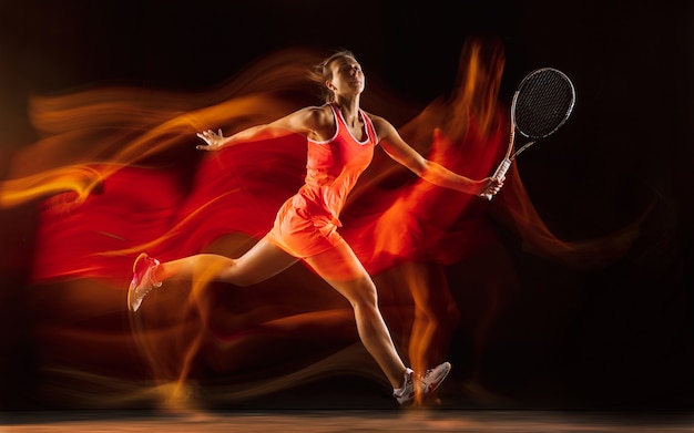 Free Photo professional female tennis player training isolated on black studio background in mixed light. woman in sportsuit practicing.