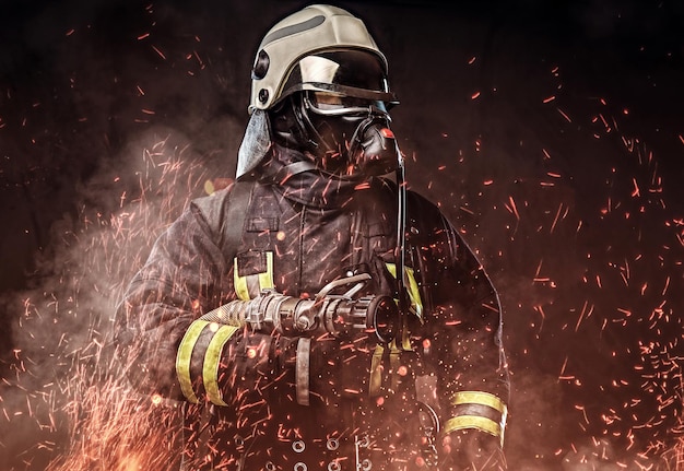 A professional firefighter dressed in uniform and an oxygen mask standing in fire sparks and smoke over a dark background.