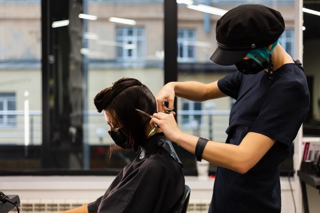 A professional girl hairdresser makes a client haircut. The girl is sitting in a mask in beauty the salon