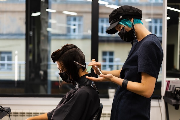 A professional girl hairdresser makes a client haircut. The girl is sitting in a mask in beauty the salon