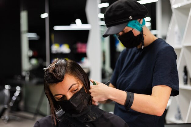 A professional girl hairdresser makes a client haircut. The girl is sitting in a mask in beauty the salon