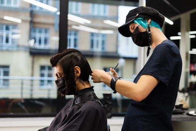 A professional girl hairdresser makes a client haircut. The girl is sitting in a mask in beauty the salon