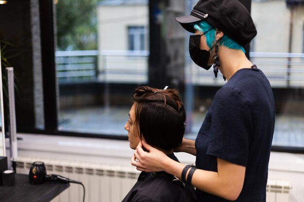 A professional girl hairdresser makes a client haircut. The girl is sitting in a mask in beauty the salon