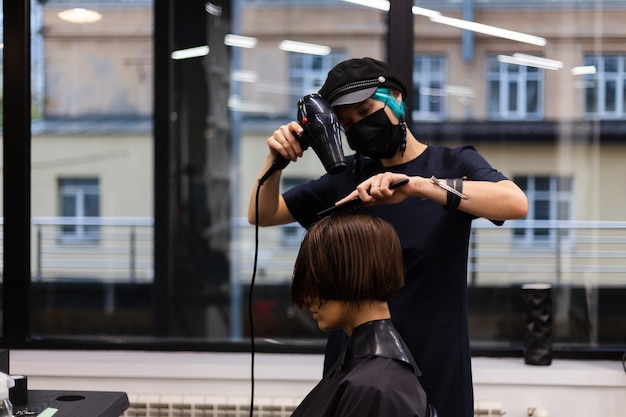 A professional girl hairdresser makes a client haircut. The girl is sitting in a mask in beauty the salon