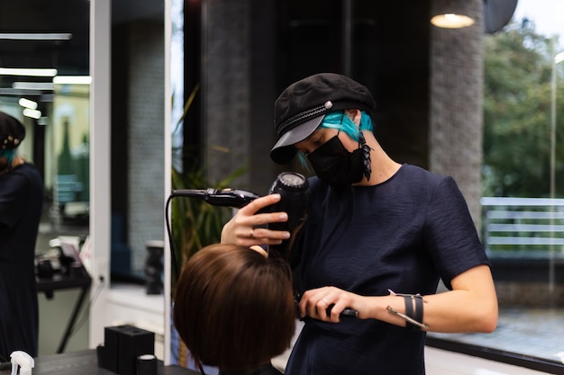 A professional girl hairdresser makes a client haircut. The girl is sitting in a mask in beauty the salon