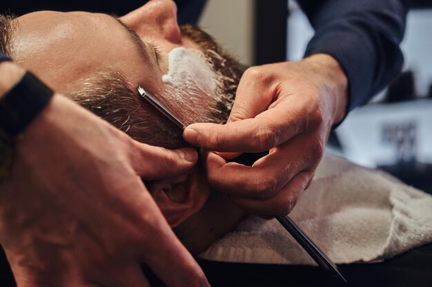 Professional hairdresser modeling beard at the barbershop. Close-up photo.