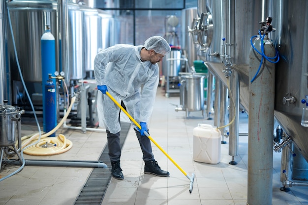 Professional industrial cleaner in protective uniform cleaning floor of food processing plant