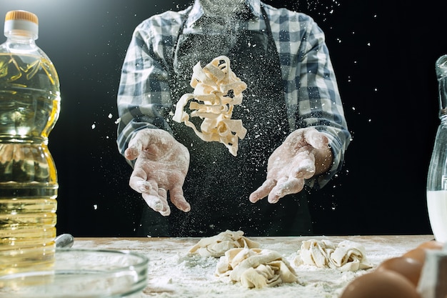 Free Photo professional male cook sprinkles dough with flour, preapares or bakes bread at kitchen table