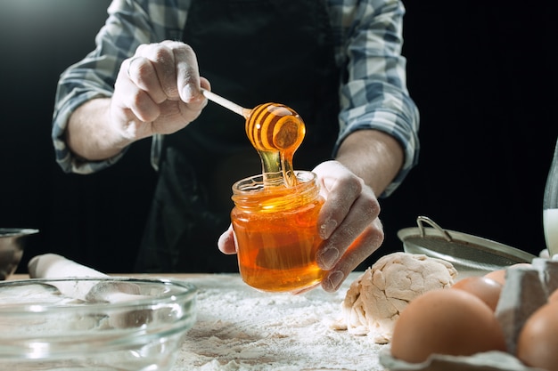 Free photo professional male cook sprinkles dough with flour, preapares or bakes bread at kitchen table