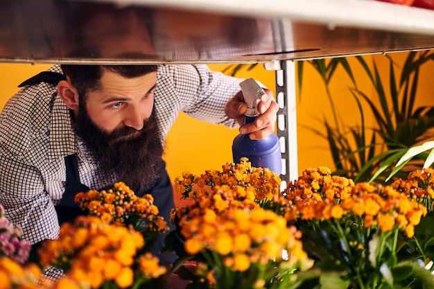 Free Photo professional male florist with beard and tattoo on his hand wearing uniform taking care of flowers in a modern flower shop.