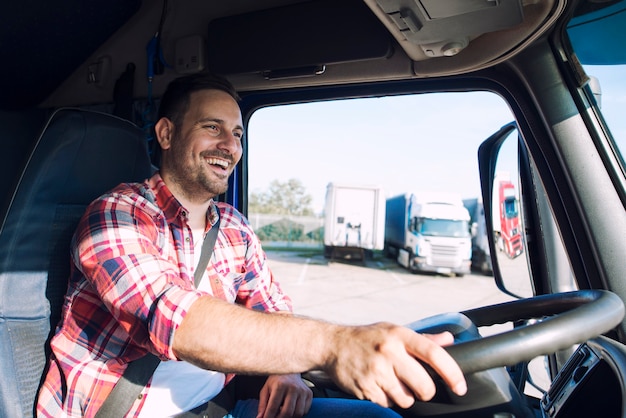 Professional middle aged truck driver in casual clothes driving truck vehicle and delivering cargo to destination