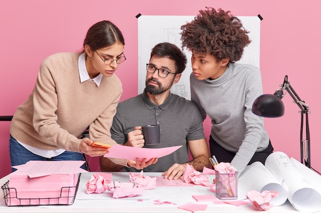 Professional mixed race experts discuss future project and blueprints during collaboration in office consult each other on important issues pose at desktop with papers around. Team work concept