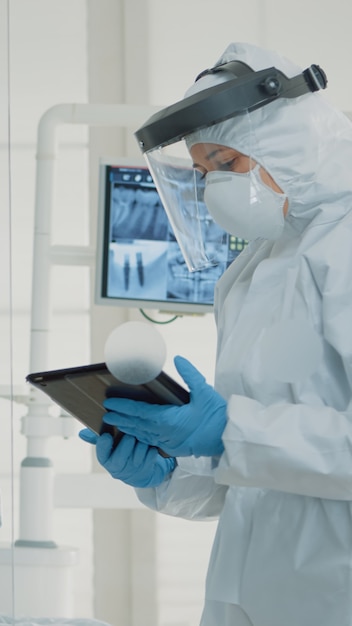 Free photo professional stomatologists using digital tablet in dental cabinet at clinic. dentist and assistant with ppe suits discussing patient oral care for operation and teeth surgery