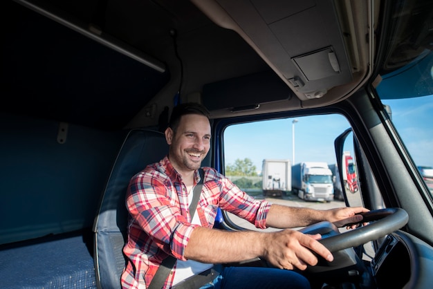 Professional truck driver in casual clothing wearing seat belt on and driving his truck to destination