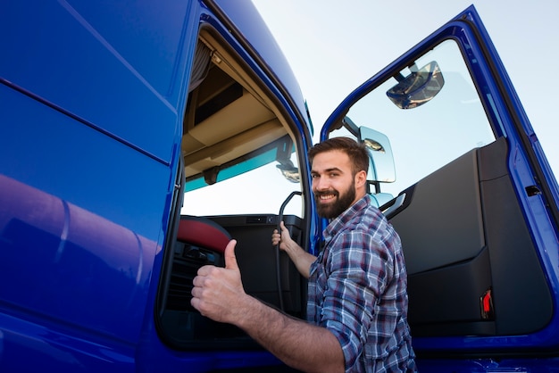 Professional truck driver entering his truck long vehicle and holding thumbs up