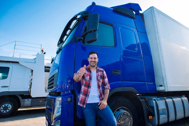 Professional truck driver in front of long transportation vehicle holding thumbs up ready for a new ride