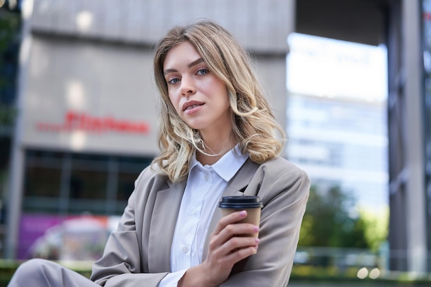 Free photo professional woman standing with coffee in a busy street smiling at camera