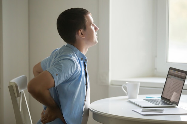 Free photo profile portrait of man at laptop, stretching, backache position