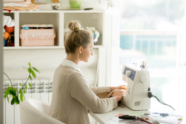 Profile portrait of a young attractive woman at sewing machine