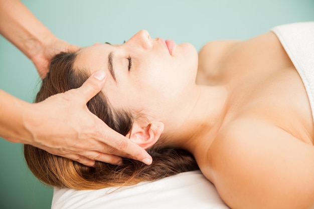 Profile view of a beautiful young woman getting a head massage by a therapist at a beauty clinic and spa