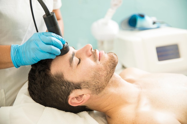 Profile view of a good looking young man getting a RF facial treatment in a health spa